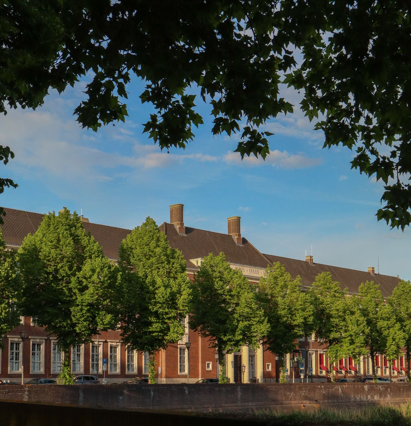Historisch gebouw aan het water in ’s-Hertogenbosch achter een rij bomen